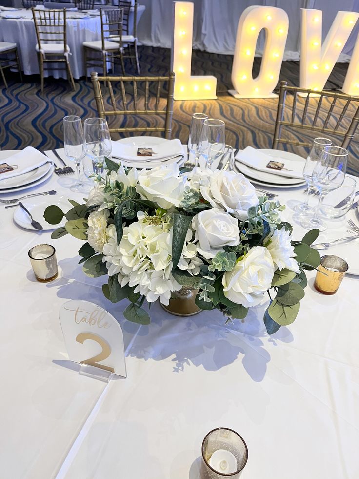 a centerpiece with white flowers and greenery sits on a table at a wedding reception