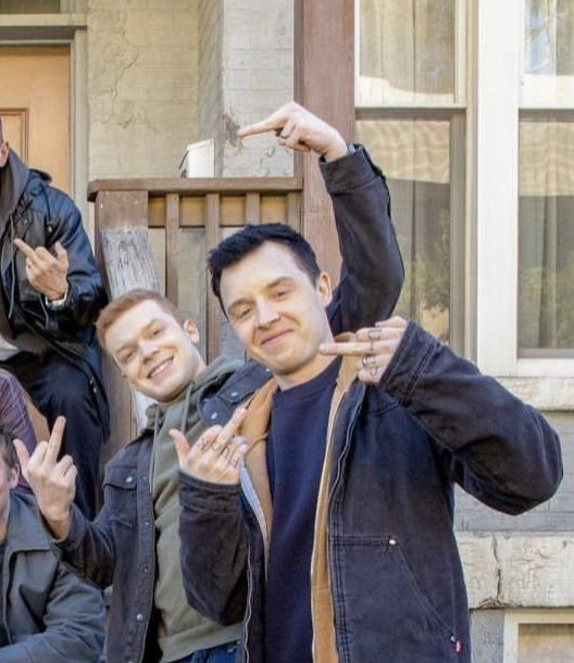 four men standing in front of a door making the peace sign with their hands and fingers