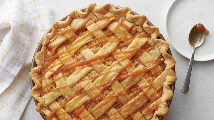 an apple pie with caramel drizzled on top and a plate next to it