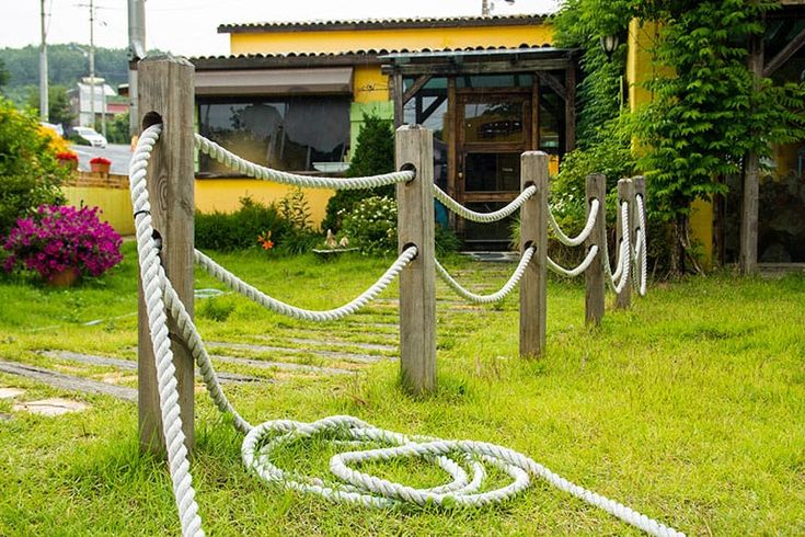 several ropes are tied to posts in the grass near a yellow building and pink flowers