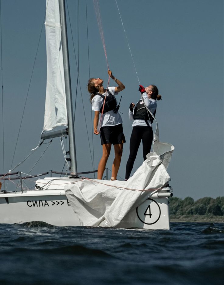 two women standing on top of a sailboat in the water