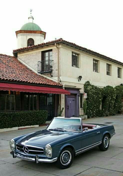 an old mercedes sits parked in front of a building with a purple door and red roof