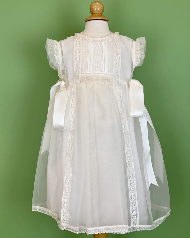 An elegant off-white dress that has a gorgeous detail in smock on the front with delicate laces. The dress has two satin ribbons on the side, and has buttons on the back for closure. Made in Spain Dry Clean Final sale, no exchanges nor returns are accepted Elegant White Dress For Confirmation, Elegant Dress With Lace Sleeves For Confirmation, Elegant Confirmation Dress With Lace Sleeves, Elegant Summer Lace Dress For First Communion, White Spring Dresses With Ribbon Detail, White Spring Dress With Ribbon Detail, White Dress With Ribbon Detail For Spring, Elegant Lace Dress For First Communion, Elegant Lace Dress With Lace Bodice For Confirmation