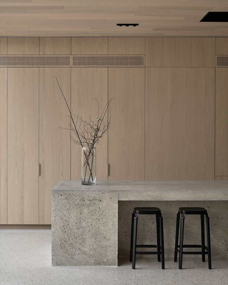 two stools sit in front of a concrete counter with flowers in a vase on it