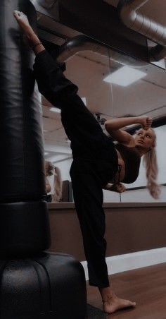 a woman standing on one leg while doing a handstand in front of a punching bag