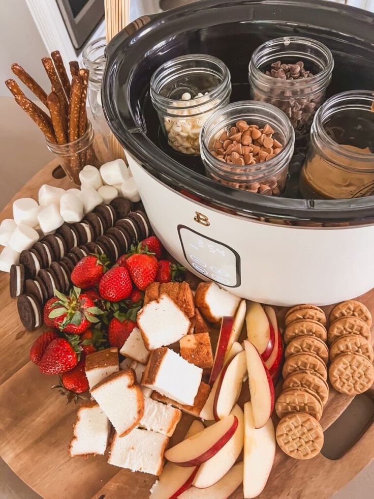 an assortment of cheeses, crackers and strawberries on a wooden table with a crock pot