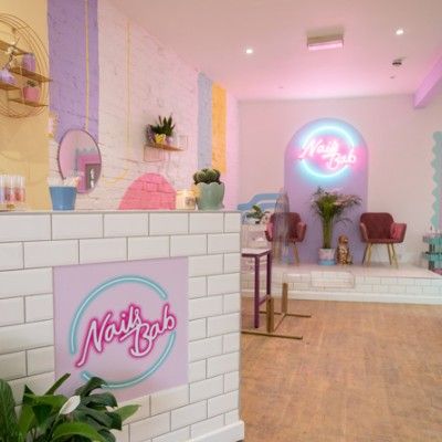 the interior of a nail salon with pink and blue walls, potted plants and neon lights