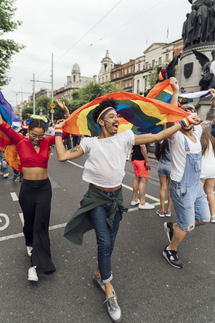 some people are walking down the street with their arms in the air and one is holding a rainbow flag