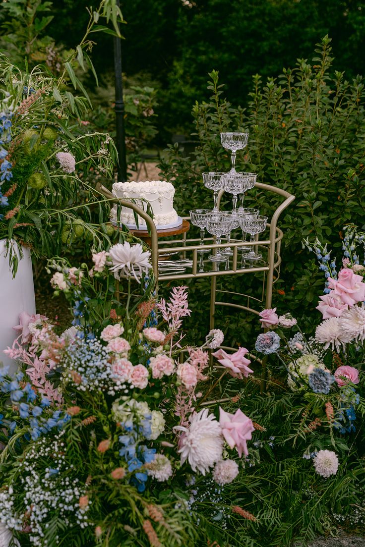 a garden filled with lots of flowers next to a chair and wine glass on top of a table