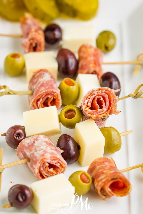 an appetizer with olives, cheese and ham on skewers next to pickles