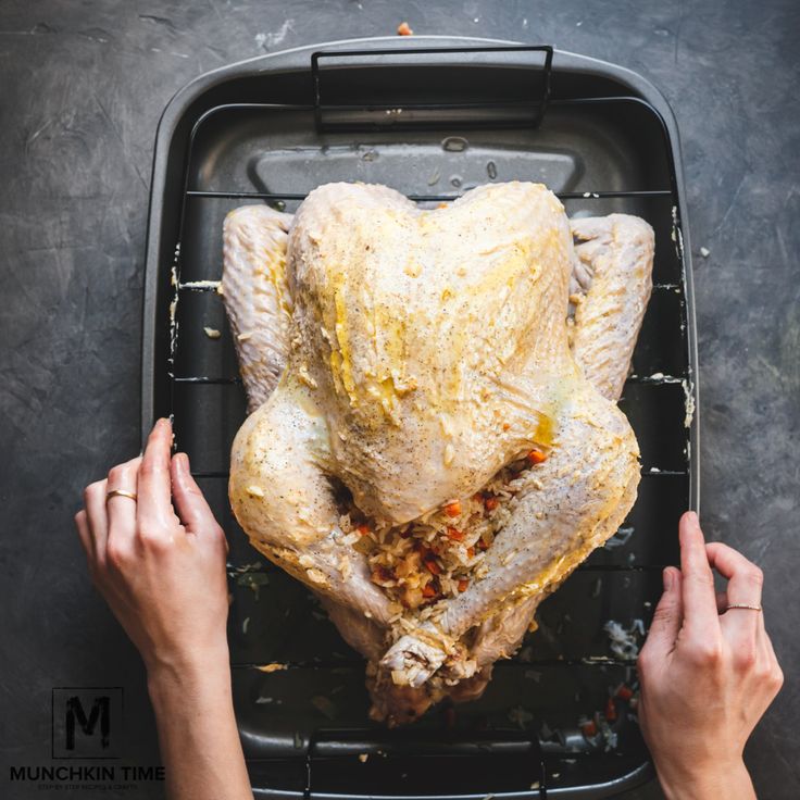 two hands holding a roasting pan with a whole chicken on it and another person's hand reaching for the turkey