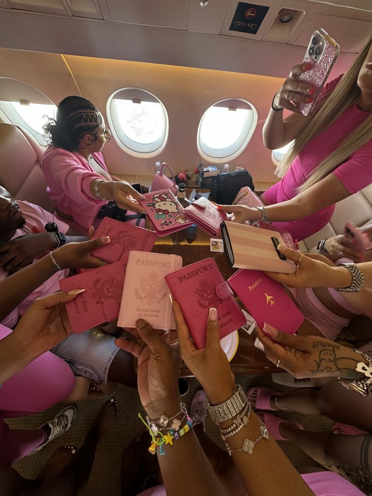 several women in pink dresses are sitting on an airplane and reaching out their hands to each other