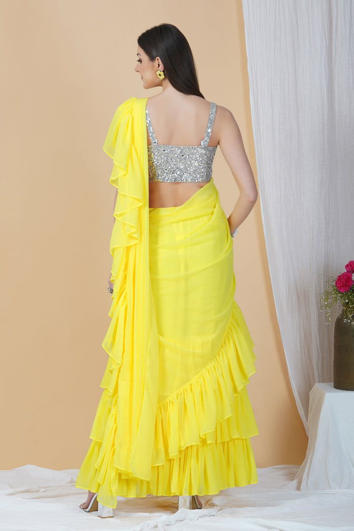 Groove at the cocktail party or a friend's wedding in this stunning frilly saree. Whimsical and lightweight, it is well paired with a contrasting strappy silver blouse that enhances the overall appeal to make it a perfect pick this season.Style Frill saree Silver embellished blouse Sunshine yellow hue Georgette fabric Specifications Model height - 5'9" Model wearing - S Elegant Summer Pre-draped Saree With Dupatta, Silver Georgette Pre-draped Saree For Wedding, Fitted Georgette Pre-draped Saree For Celebration, Glamorous Georgette Pre-draped Saree For Celebration, Glamorous Pre-draped Saree With Ruffles For Festive Occasions, Bollywood Style Pre-draped Saree With Sheer Dupatta For Summer, Summer Pre-draped Saree With Zari Work For Reception, Summer Wedding Georgette Blouse Piece, Party Pre-draped Georgette Saree With Cutdana