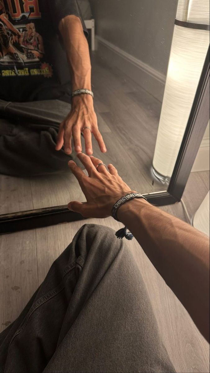 a man is sitting on the floor with his hands in front of him while holding onto a mirror