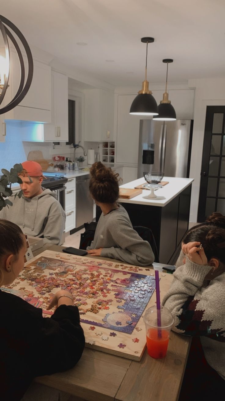 four people sitting at a kitchen table playing a board game with orange juice in front of them