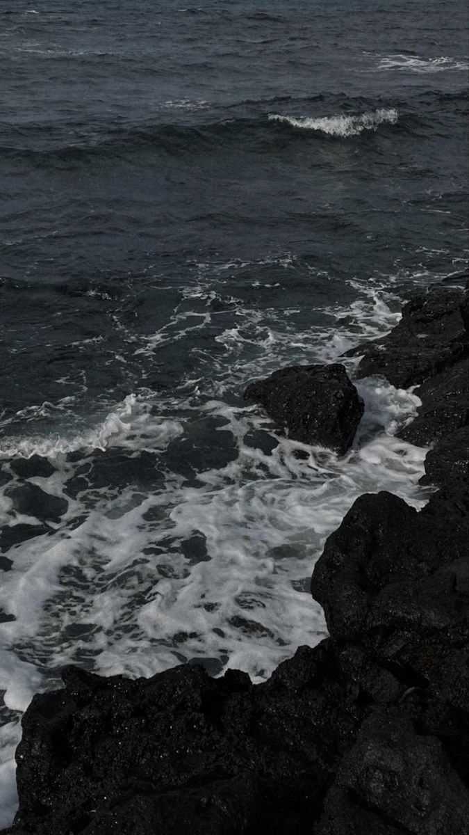 an ocean view with waves crashing on the rocks and dark clouds in the sky above