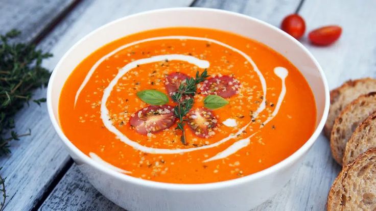 a bowl of tomato soup with bread on the side