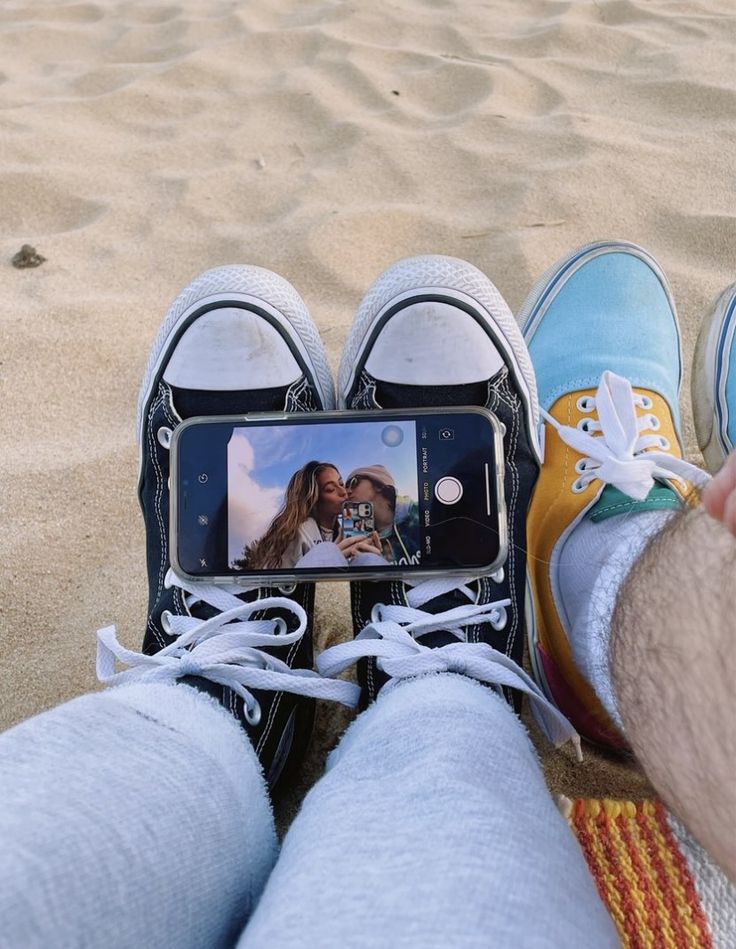 someone is taking a photo with their cell phone on the beach while sitting in the sand