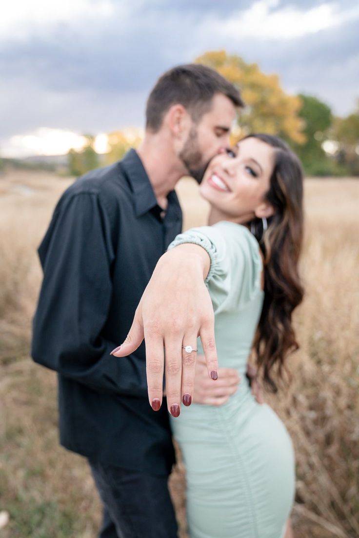 a man and woman standing in a field with their hands on each other's shoulders