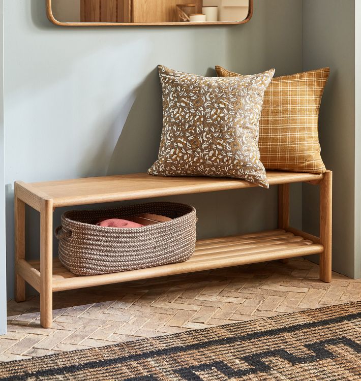 a wooden bench sitting next to a wall with pillows on top of it and a mirror above it