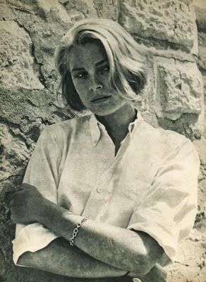 black and white photograph of a woman leaning against a stone wall with her arms crossed