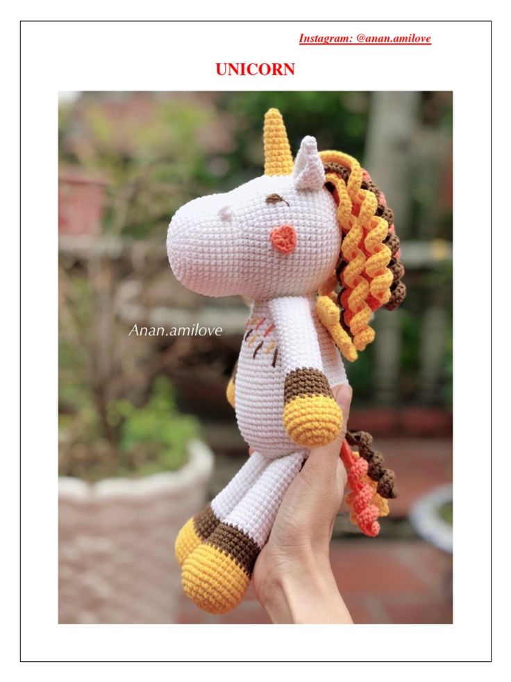 a crocheted stuffed unicorn is held up in the air by someone's hand