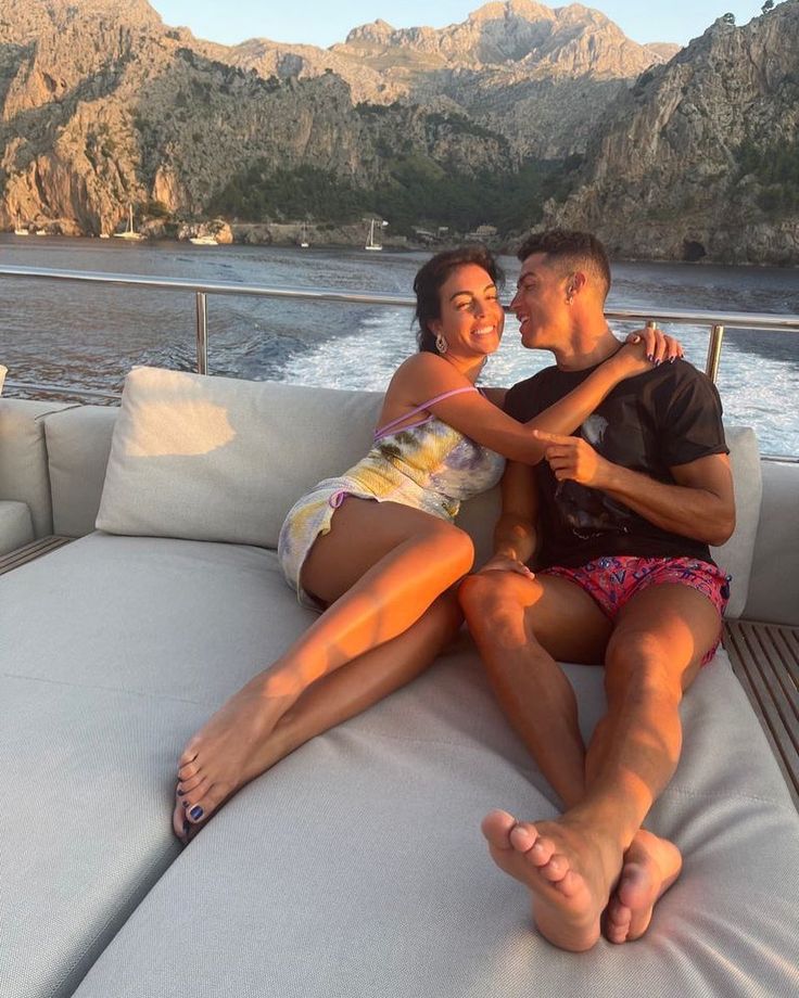 a man and woman sitting on the back of a boat with mountains in the background