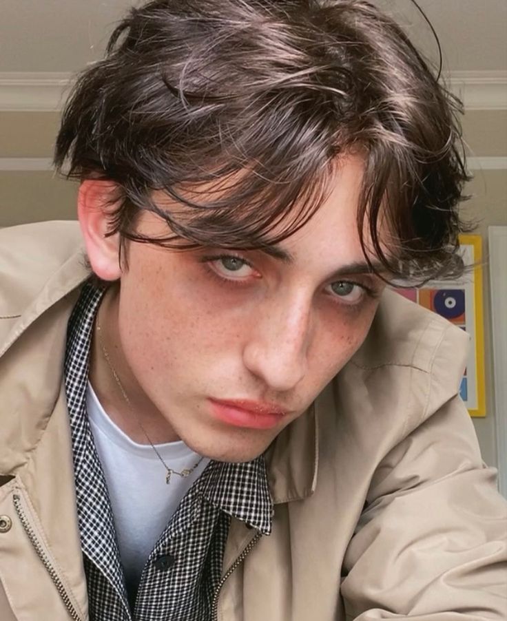 a young man wearing a trench coat and looking at the camera with serious expression on his face