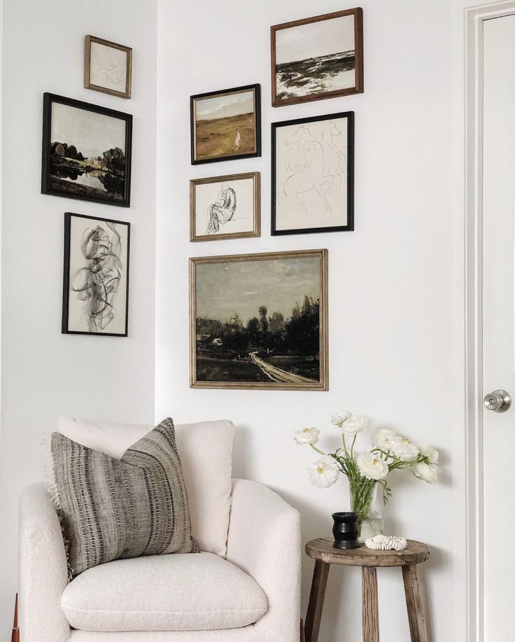 a living room with white walls and pictures on the wall above the chair is a small table with flowers in it