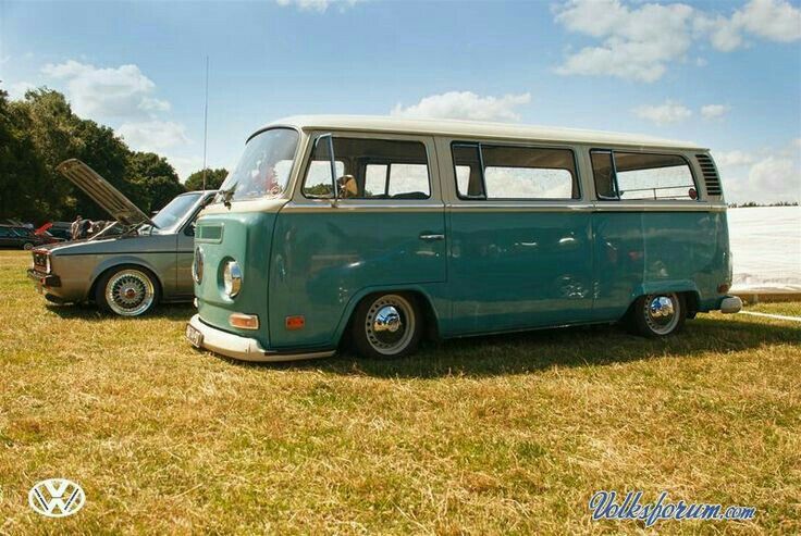 an old vw bus is parked in the grass next to another van that has it's doors open