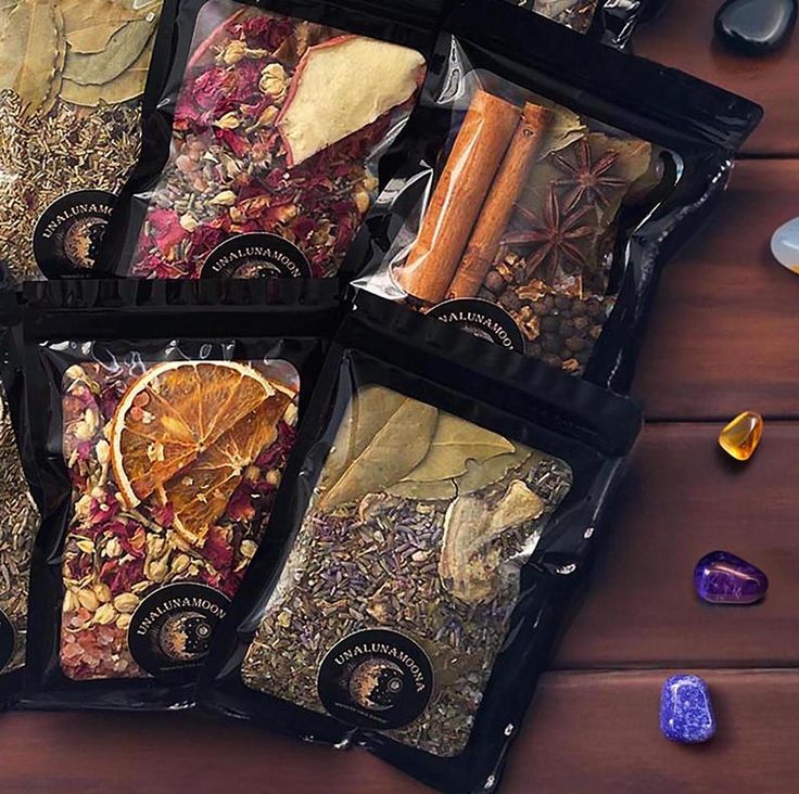 five bags of dried herbs and spices on a wooden table next to rocks, stones and crystals