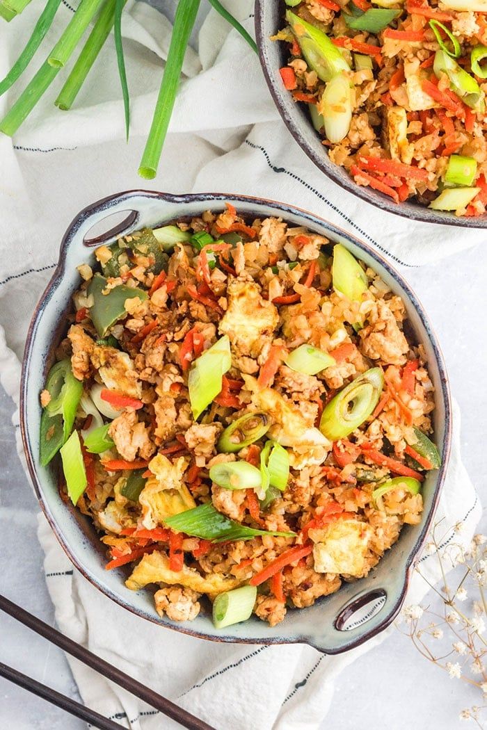 two bowls filled with rice and vegetables next to chopsticks on a white surface