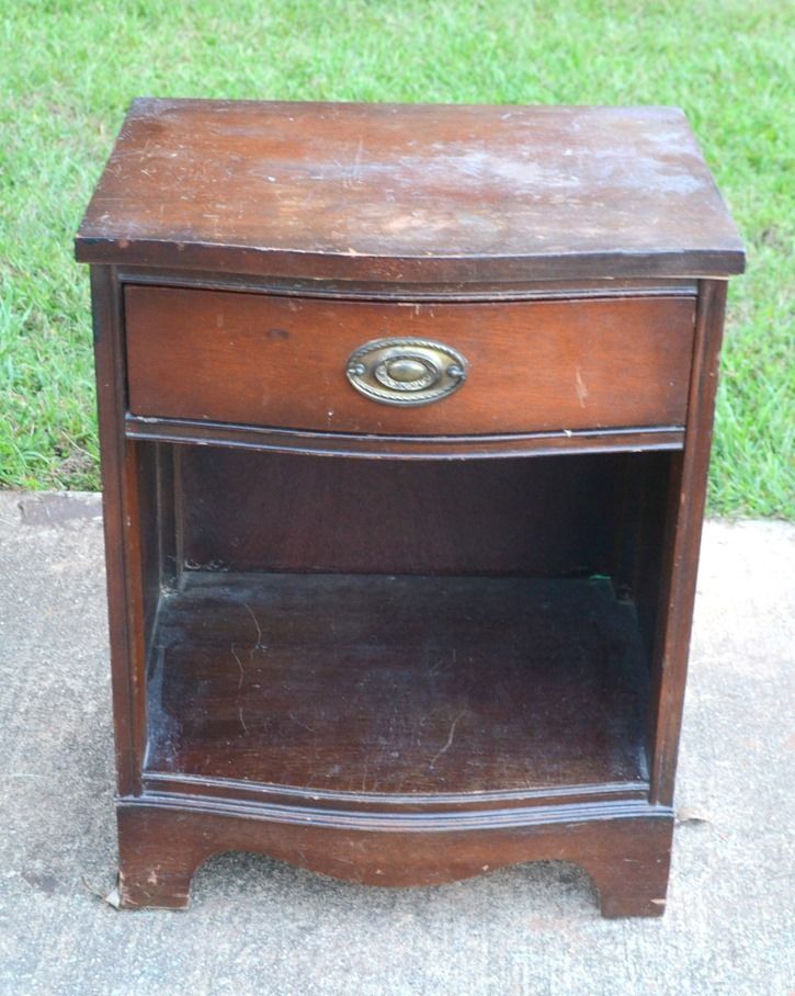 an old wooden night stand sitting on the sidewalk in front of some green grass and trees