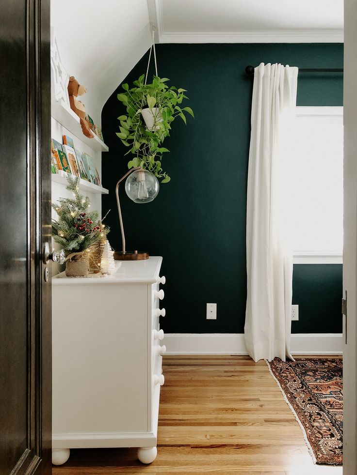 a room with green walls and wooden floors, white furniture and plants on the shelf