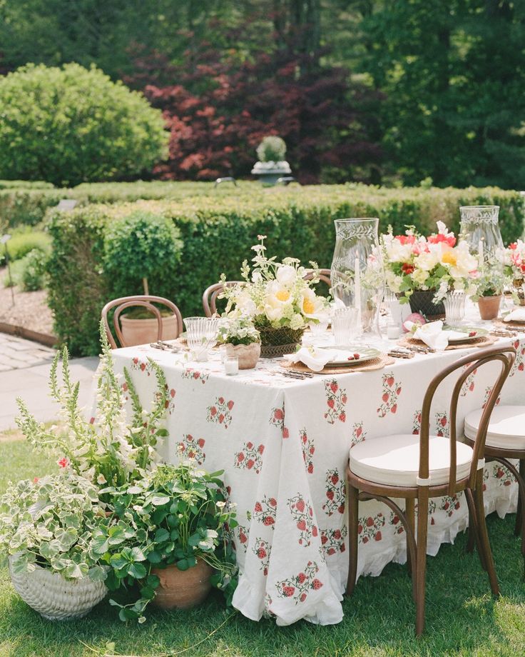 a table set up with flowers and greenery for a formal dinner in the garden