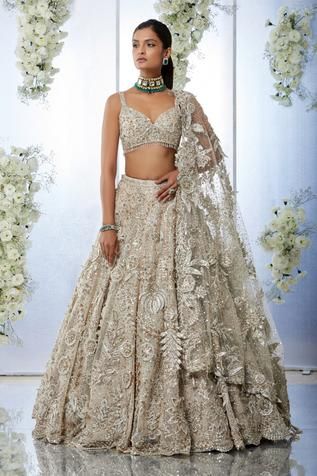 Beige lehenga features three-dimensional floral, sequin, pearl and crystal embroidery. Paired with a sweetheart neck blouse and a jaal embroidered net dupatta. 
Component: 3
Pattern: Embroidered
Type Of Work: Floral
Neckline: Sweetheart
Sleeve Type: Sleeveless
Fabric: Net
Color: Beige
Other Details: 
Floral embroidery
Tassel detail
Back tie-up
Embroidered dupatta
Occasion: Wedding, Bride - Aza Fashions Gold Reception Lengha, Reception Lengha Bridal, Shaadi Lehnga, Nude Lehenga, Reception Lengha, Gold Lengha, Hall Construction, Beige Lehenga, Sweetheart Neck Blouse