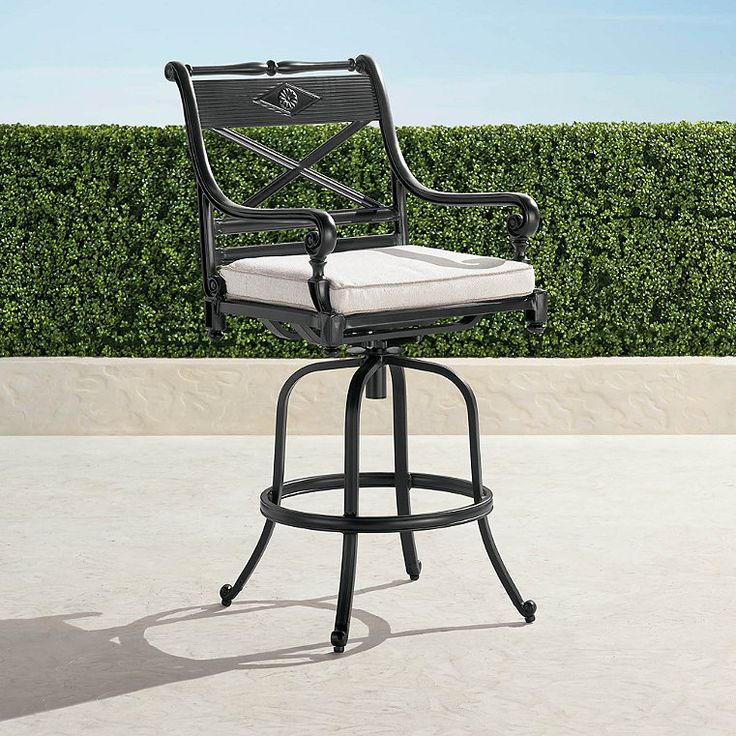 an outdoor bar stool with a cushion on the back and seat, in front of a hedge