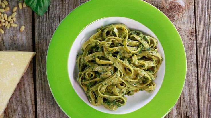 a plate of pasta with pesto and pine nuts next to it on a wooden table