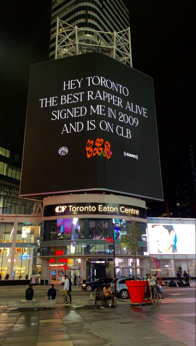 a large billboard on the side of a building with people walking around it at night