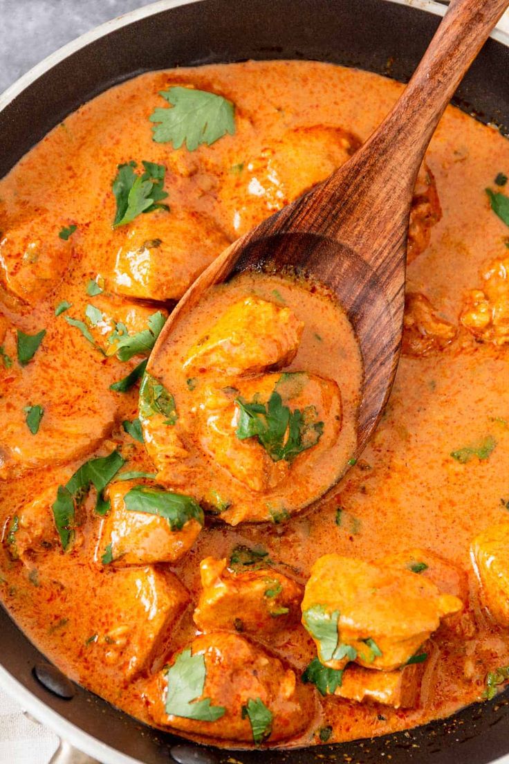 a wooden spoon in a pot filled with chicken and tomato sauce on top of a table