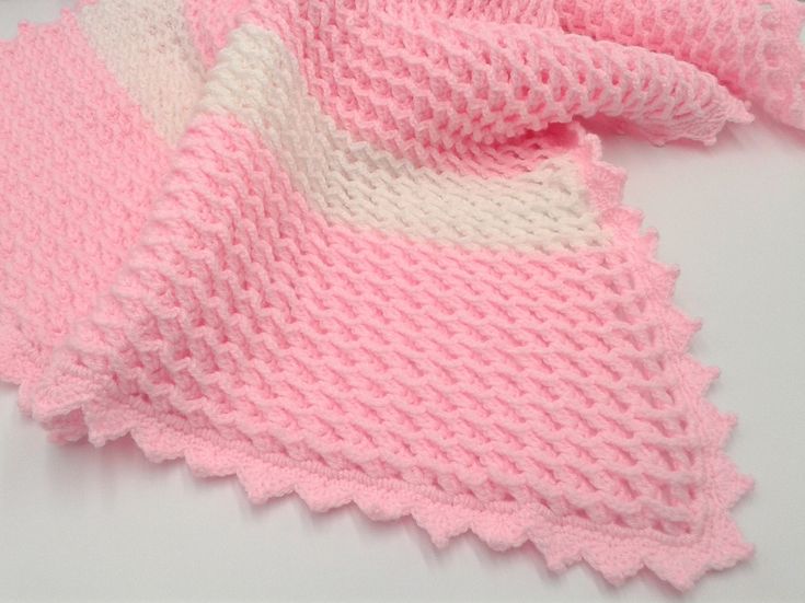 a pink and white knitted blanket laying on top of a table