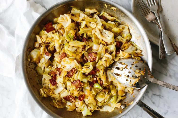 a pan filled with pasta and vegetables on top of a white table cloth next to utensils