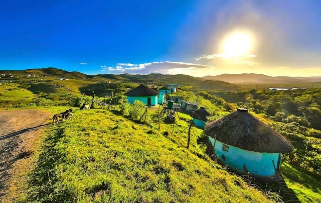 an aerial view of some huts on a grassy hill with the sun in the background