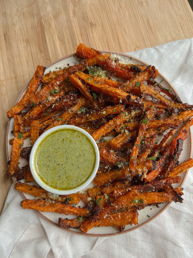 a white plate topped with fried carrots next to a bowl of dipping sauce