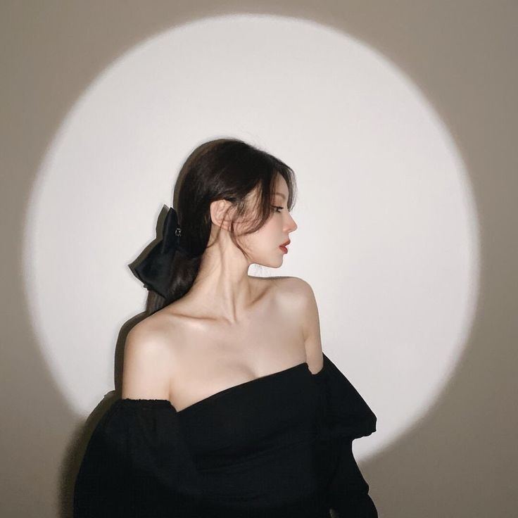 a woman wearing a black dress with a bow in her hair standing next to a white wall