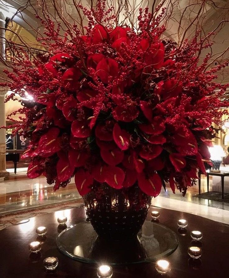 a vase filled with lots of red flowers on top of a table next to candles