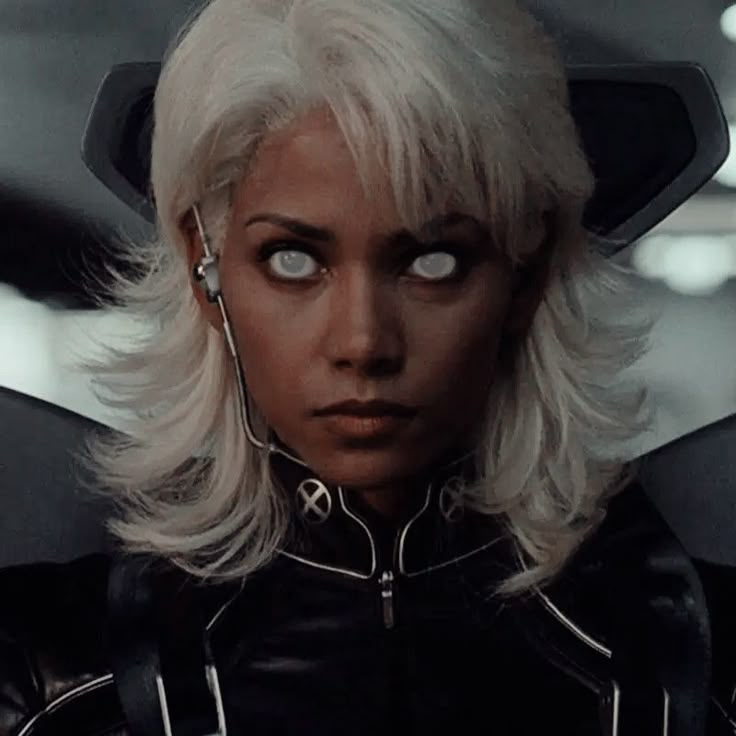 a woman with blonde hair and blue eyes in a black leather outfit looking at the camera