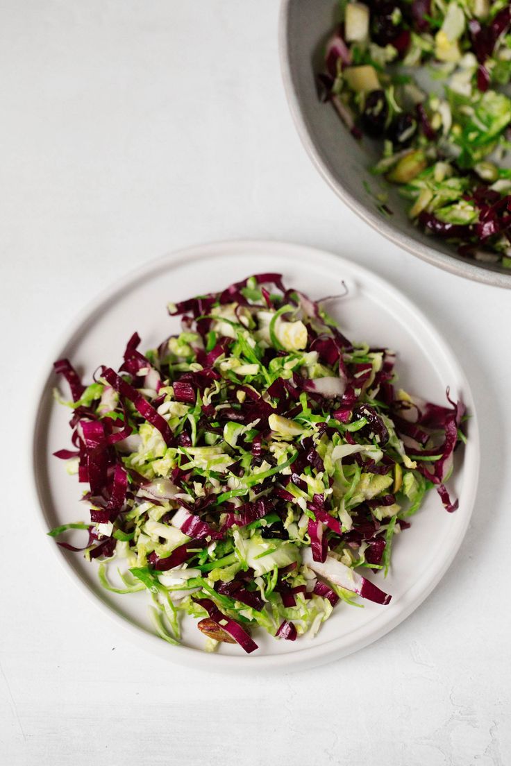 a white plate topped with salad next to a bowl