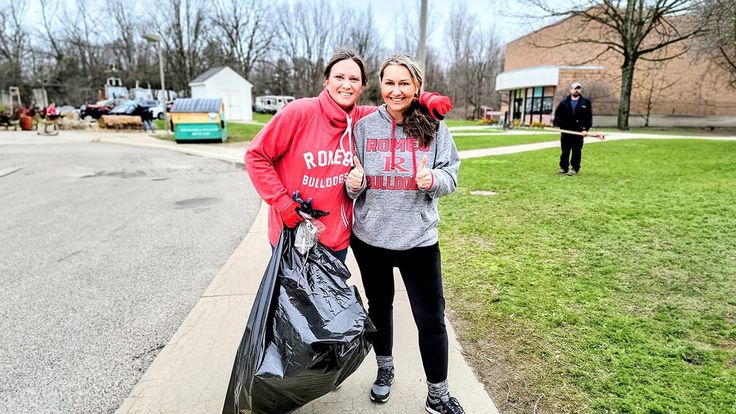 two people standing on the sidewalk with trash bags