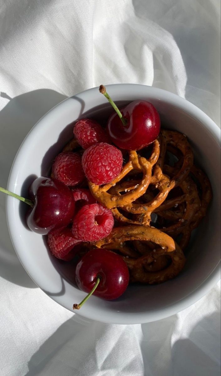 a bowl filled with cherries and pretzels on top of a white cloth